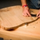 Handwerker formt einen Gitarren-Korpus aus Holz mit einem Multitool, Holzspäne auf dem Arbeitstisch, handwerkliche Arbeit in der Werkstatt.
